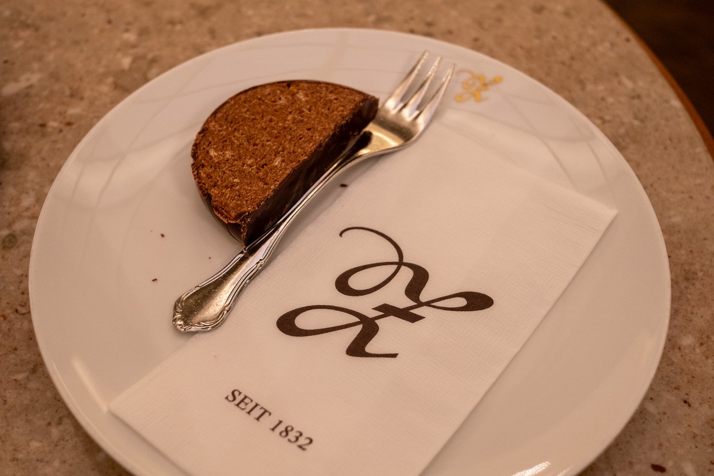 Close view of a slice of chocolate-dipped Zaunerstollen with a silver cake fork, resting on a white napkin printed with the Zauner monogram and the words SEIT 1832.