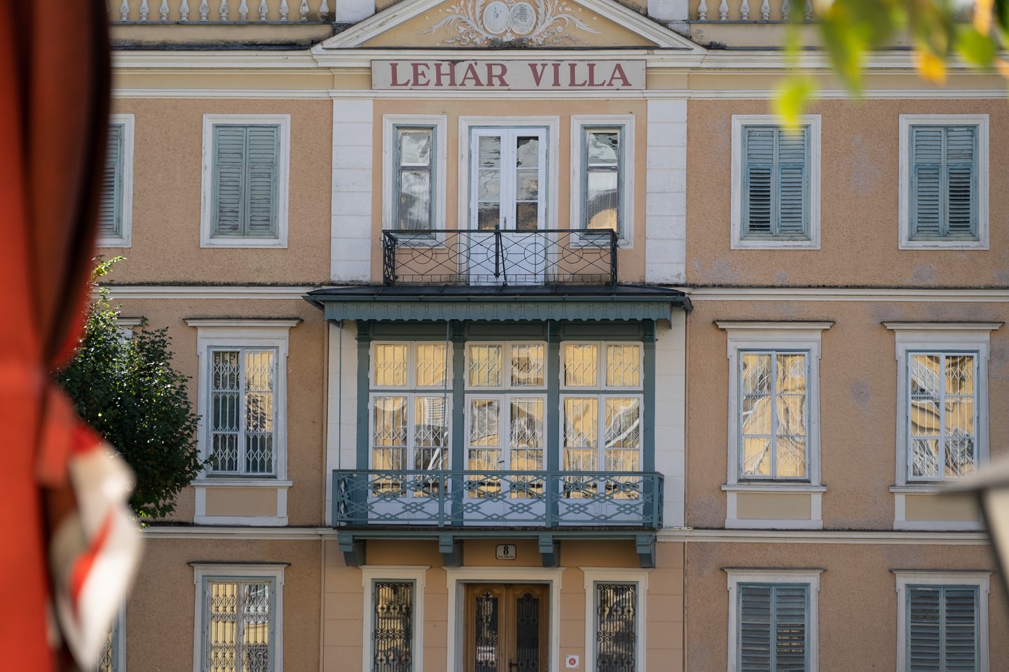 The centre of the Lehar Villa in Bad Ischl in close view, with its glazed green veranda, iron and timber balconies and the red painted LEHAR VILLA lettering under the gable.