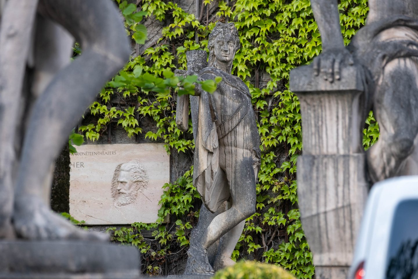 Classical stone figure and Marionettentheater relief with portrait medallion on the ivy wall in Salzburg.