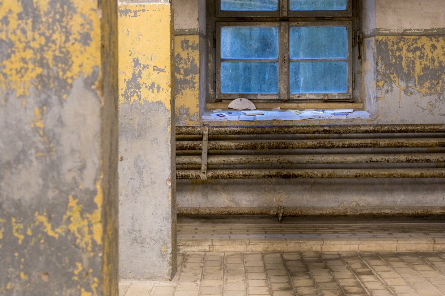 Notes, cards and photographs left by visitors on a window sill above the rusted pipe radiators in the shower room at Mauthausen.