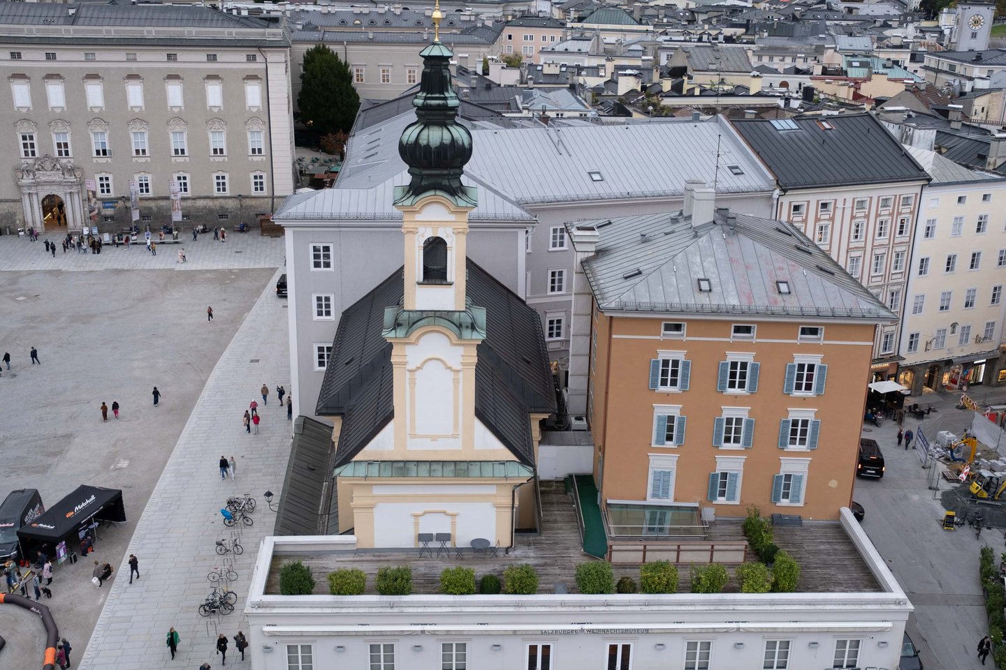 Aerial view of the Michaelskirche with green dome on Residenzplatz with event tent and walking visitors in Salzburg