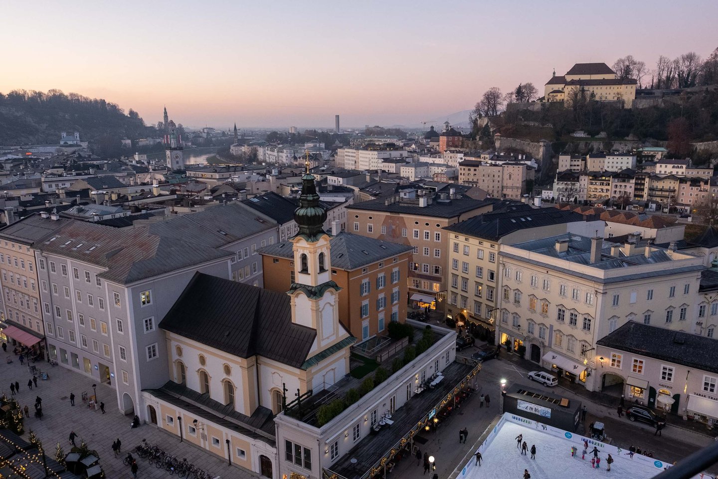 Michaelskirche on Residenzplatz with open-air ice rink and Hohensalzburg Fortress beyond in Salzburg