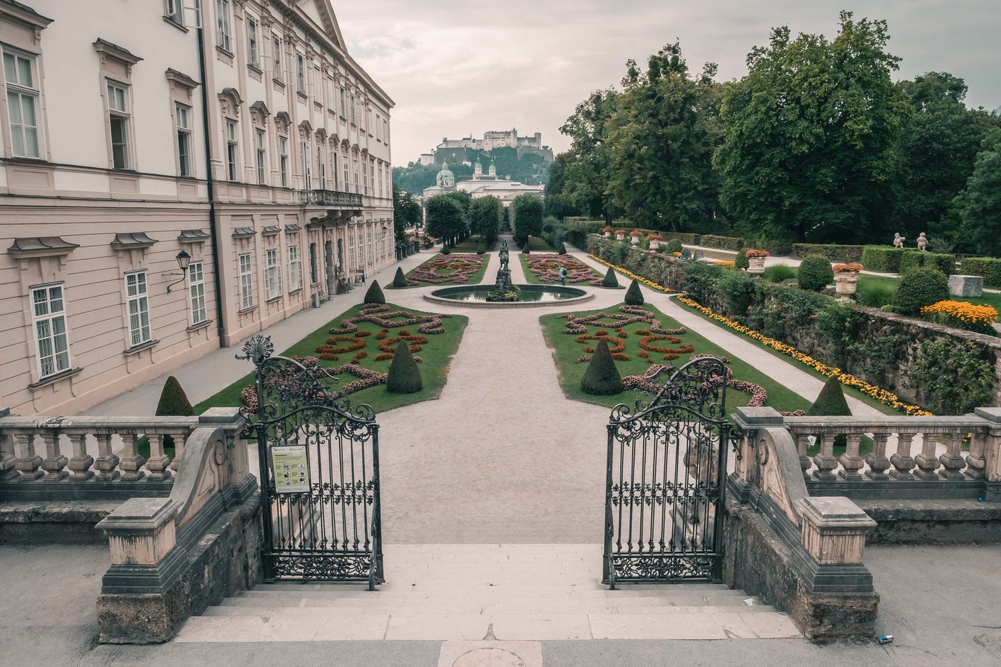 Wrought iron gate leading into Mirabell Gardens with Hohensalzburg Fortress in the distance in Salzburg.