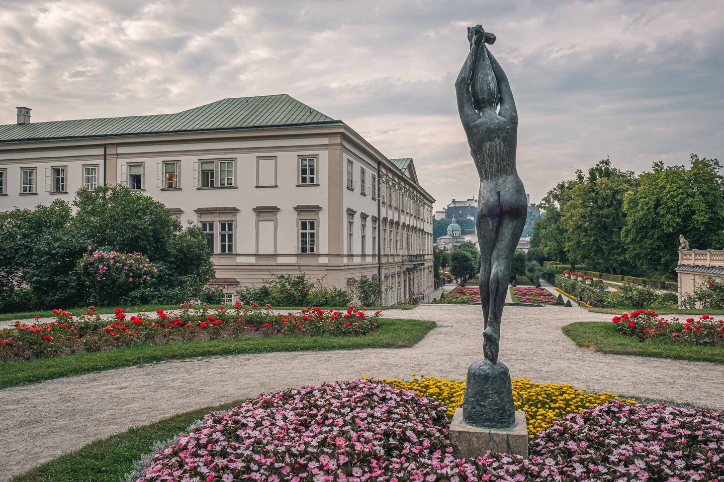 Bronze dancer sculpture among red flowerbeds in Mirabell Gardens with Mirabell Palace behind in Salzburg.