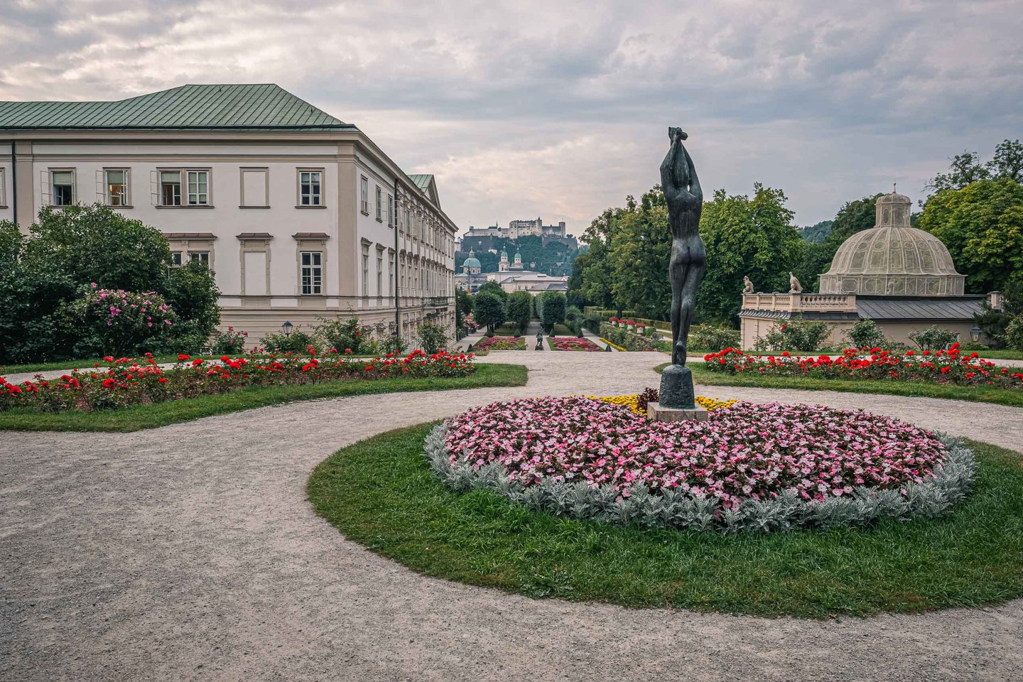 Mirabell Gardens flowerbed and bronze figure frame the view toward Hohensalzburg Fortress in Salzburg.