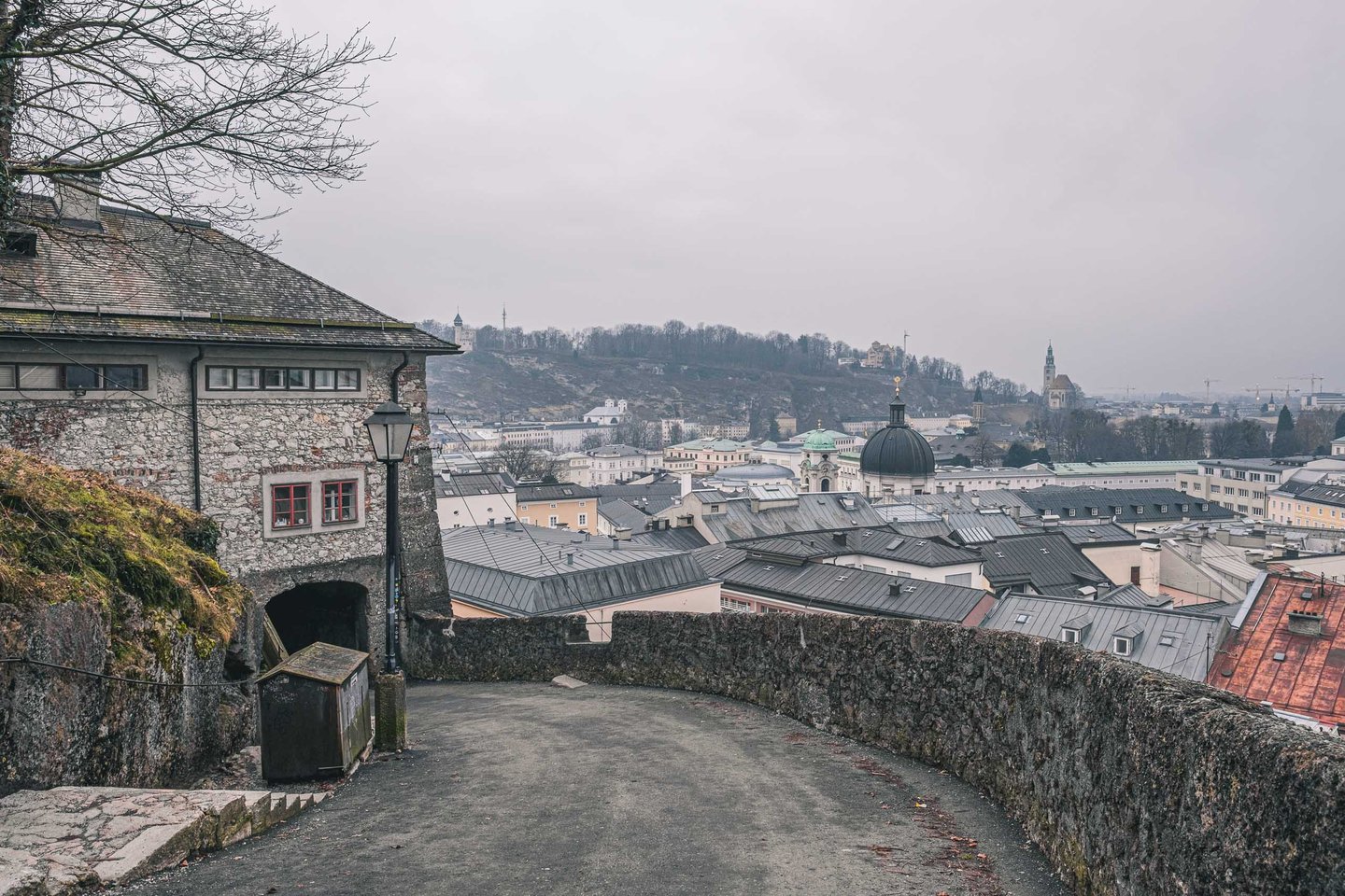 Cobblestone Moenchsberg path with stone wall on the right and view over the Salzburg old town with cathedral domes in the distance