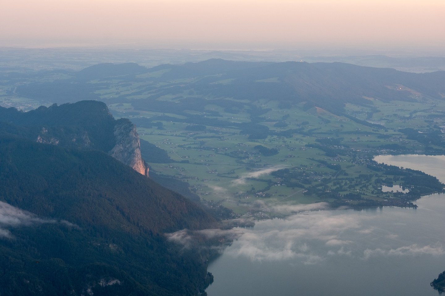 The Mondsee basin at first light seen from the Schafberg, mist lying along the water, the town of Mondsee on the far shore and the sunlit Drachenwand rising on the left.