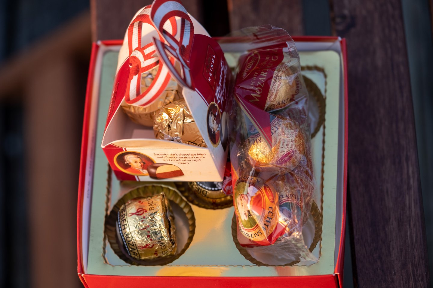 Looking down into an open red gift box holding Mozartkugeln from Heindl, Mirabell and Reber in their paper cups and cellophane sleeves.
