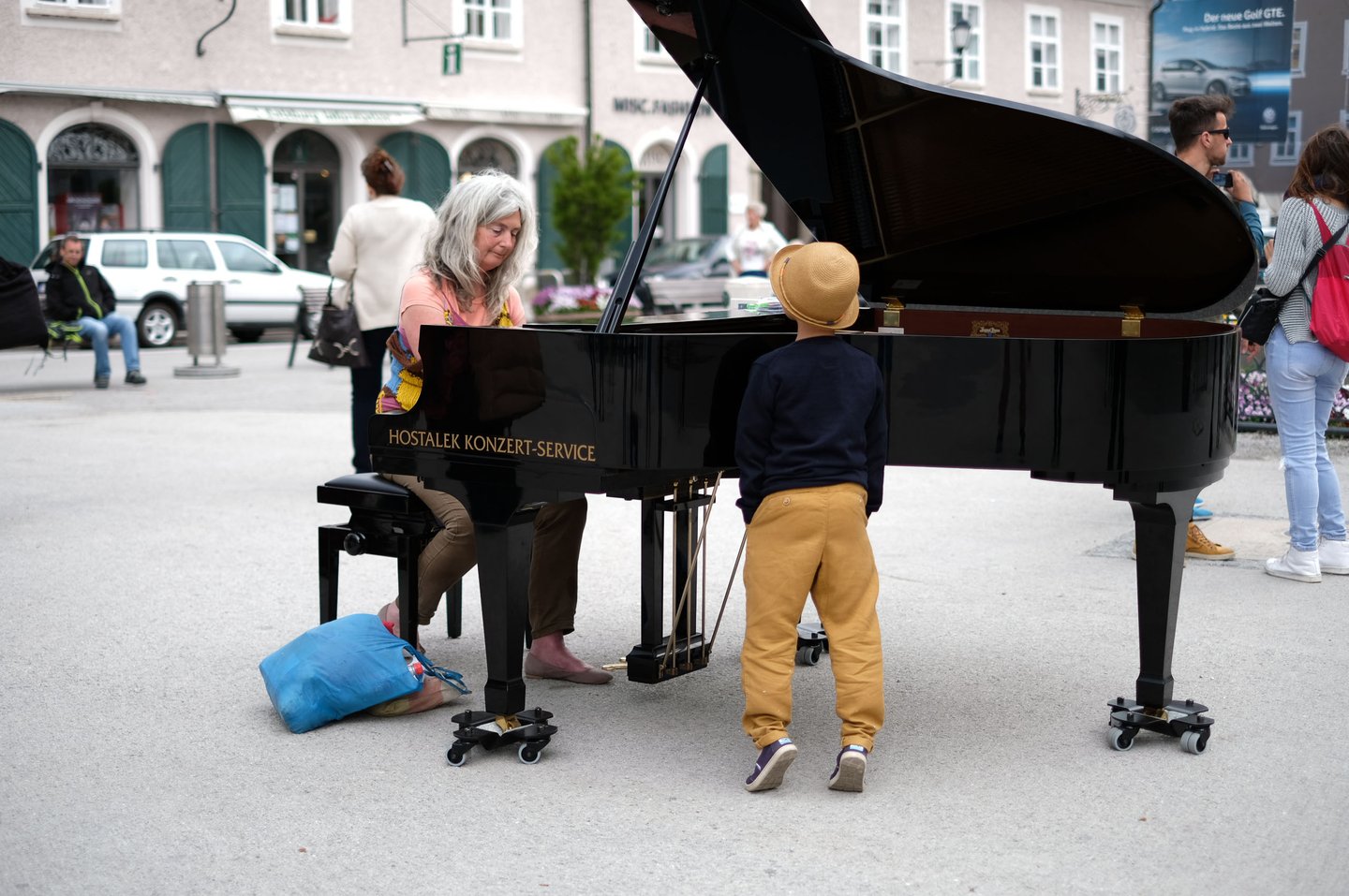 Woman plays a public grand piano as a child watches on Mozartplatz in Salzburg old town