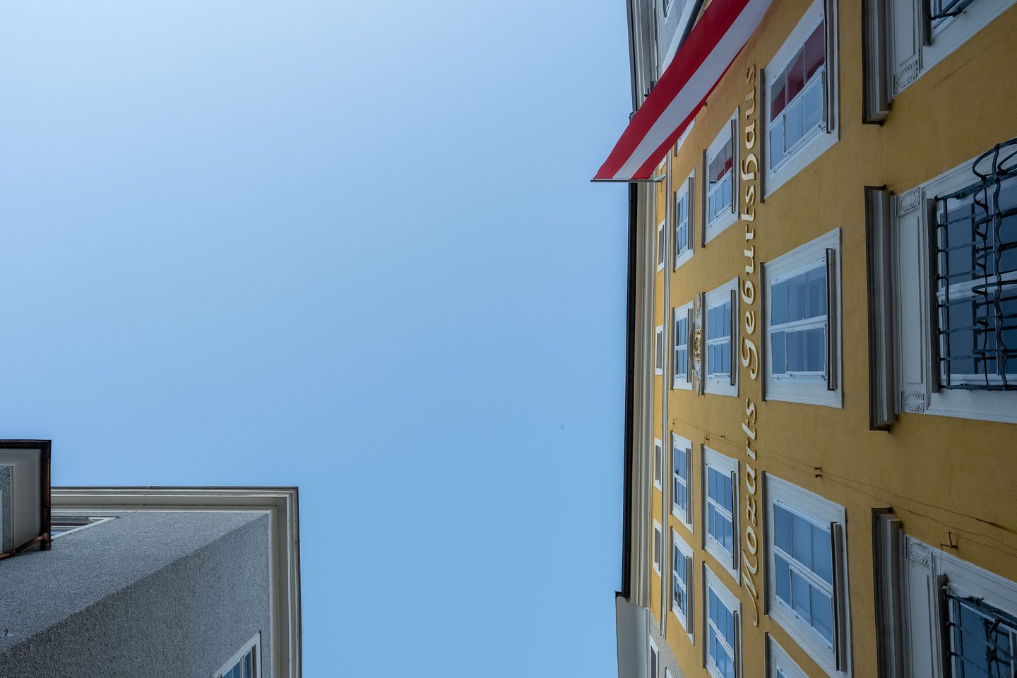 Yellow facade of Mozarts Geburtshaus with Austrian flag seen from below in Salzburg old town.