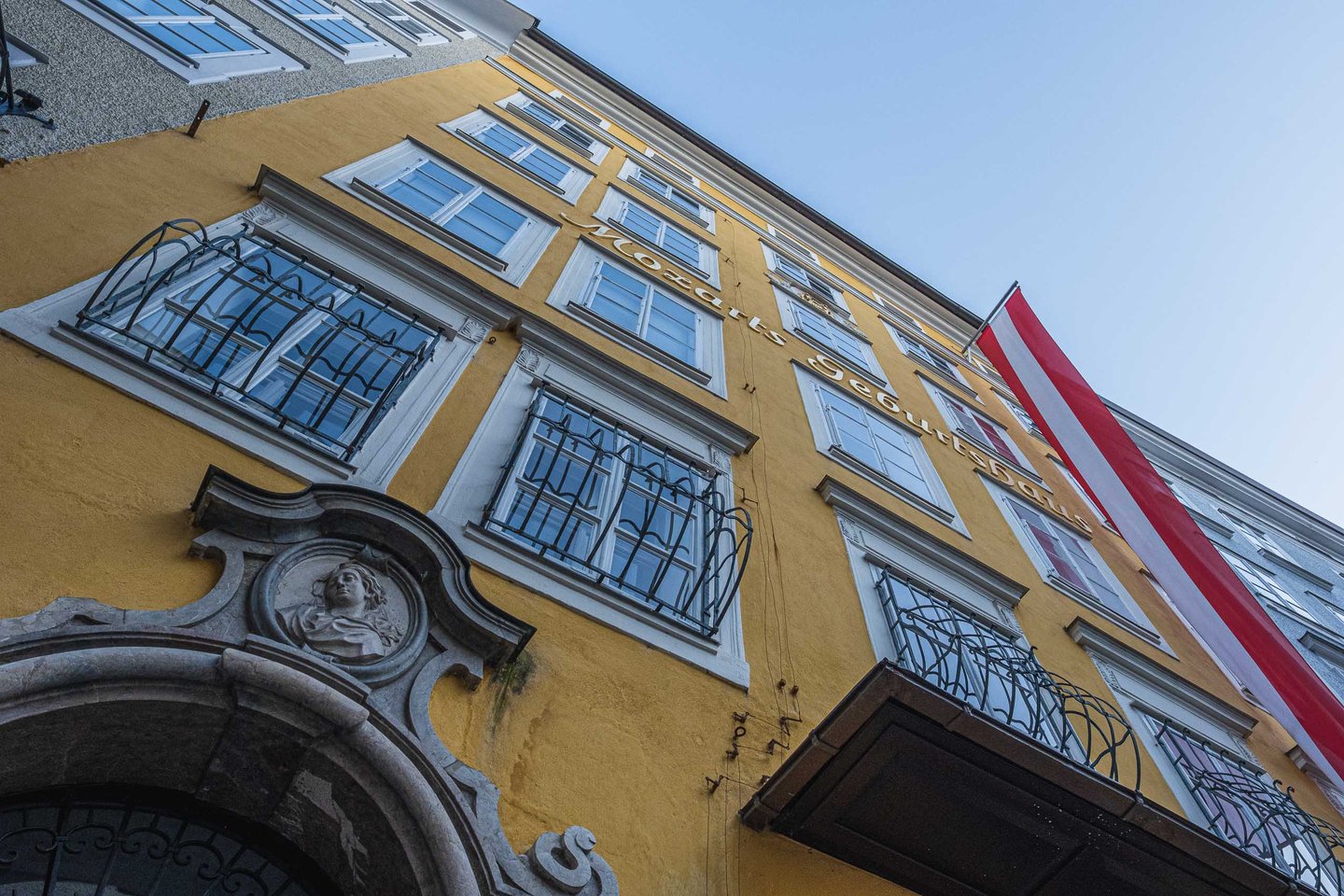 Low angle view of Mozarts Geburtshaus facade with portrait relief and Austrian flag in Salzburg.