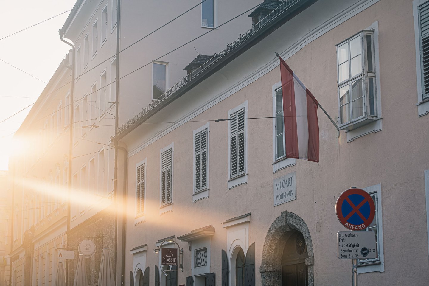 Facade of Mozart Wohnhaus with Austrian flag lit by sunrise on Makartplatz in Salzburg.