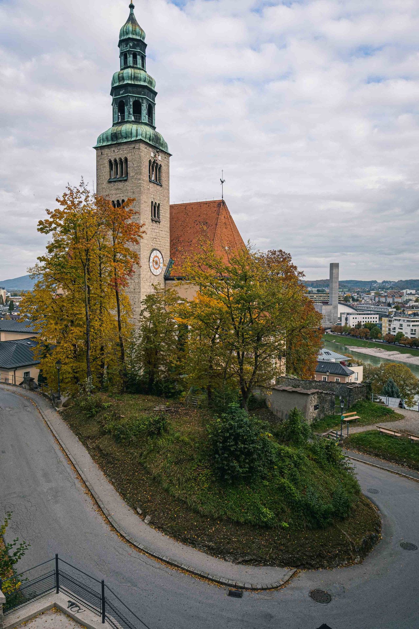 Muelln Church exterior with brick facade and green tower rises above autumn trees in Salzburg.