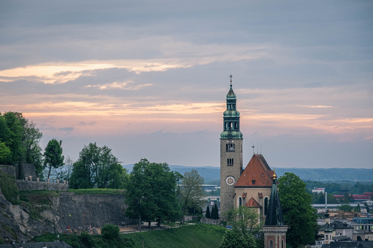 Muelln Church tower glows at sunset seen in telephoto from Kapuzinerberg in Salzburg.