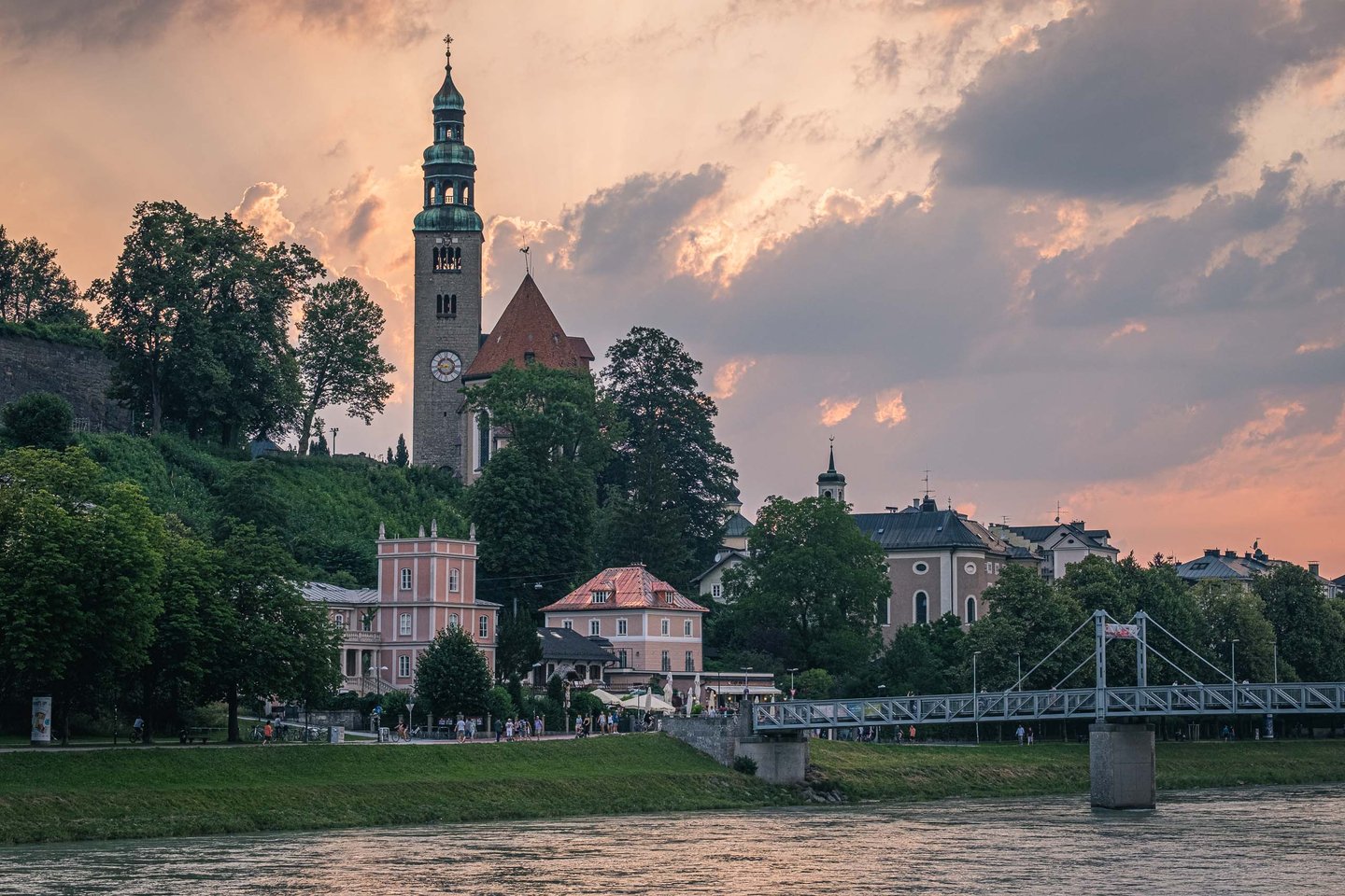 Mulln Church tower rising above riverside houses at sunset by the Salzach river in Salzburg