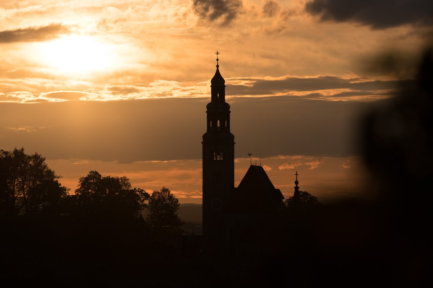 Silhouette of an onion domed church tower against an orange sunset sky in Salzburg.