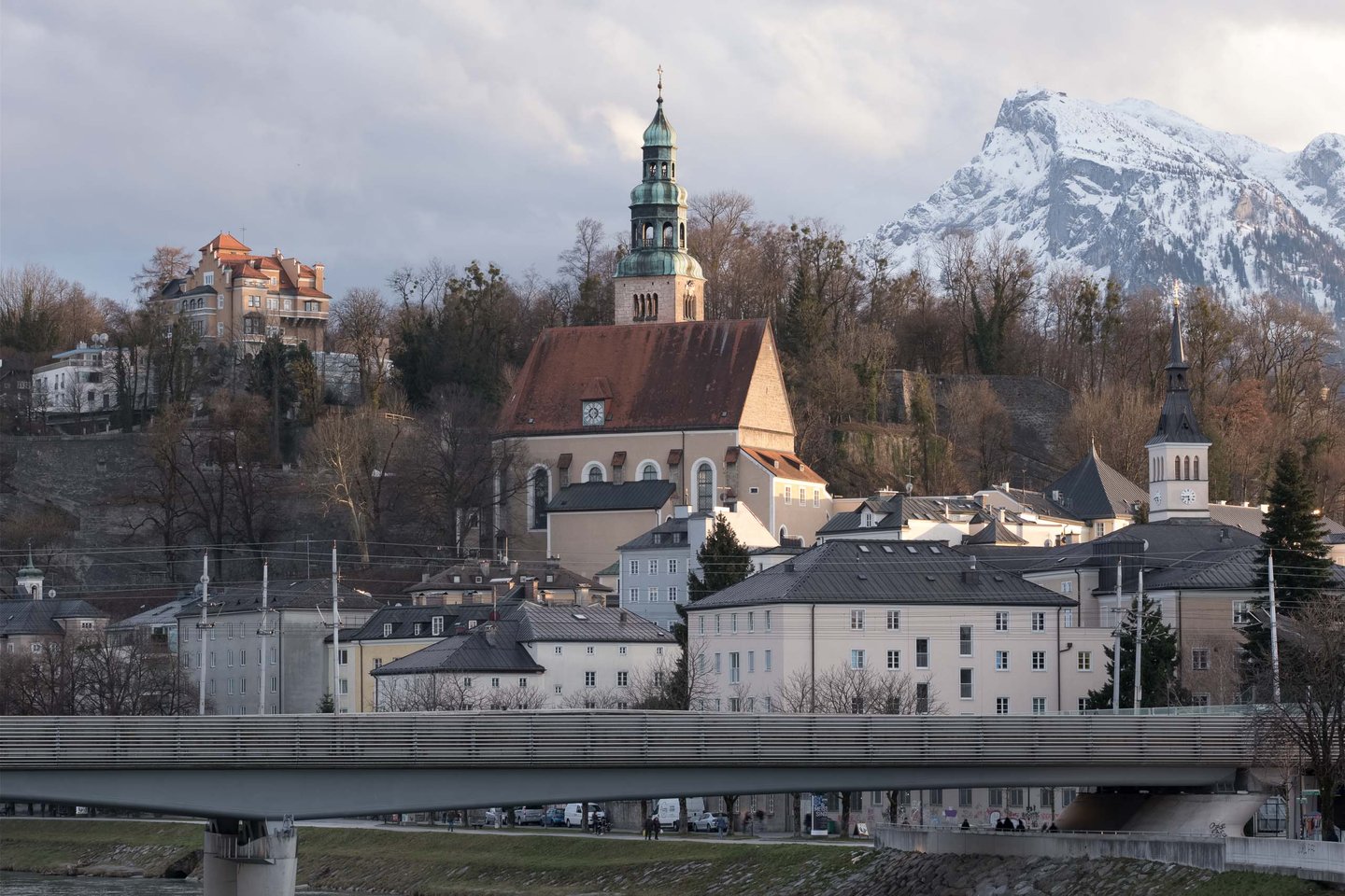 Mülln Church with its distinctive tower stands before the snow-capped Untersberg in Salzburg.