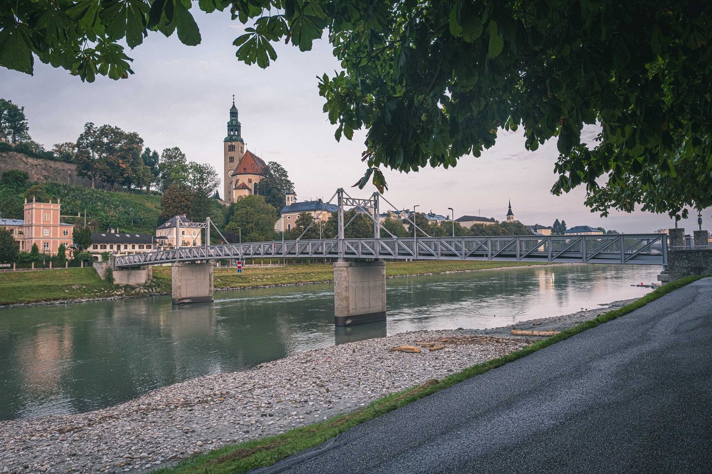 Müllnersteg pedestrian bridge crosses the Salzach beneath Mülln Church at dawn in Salzburg