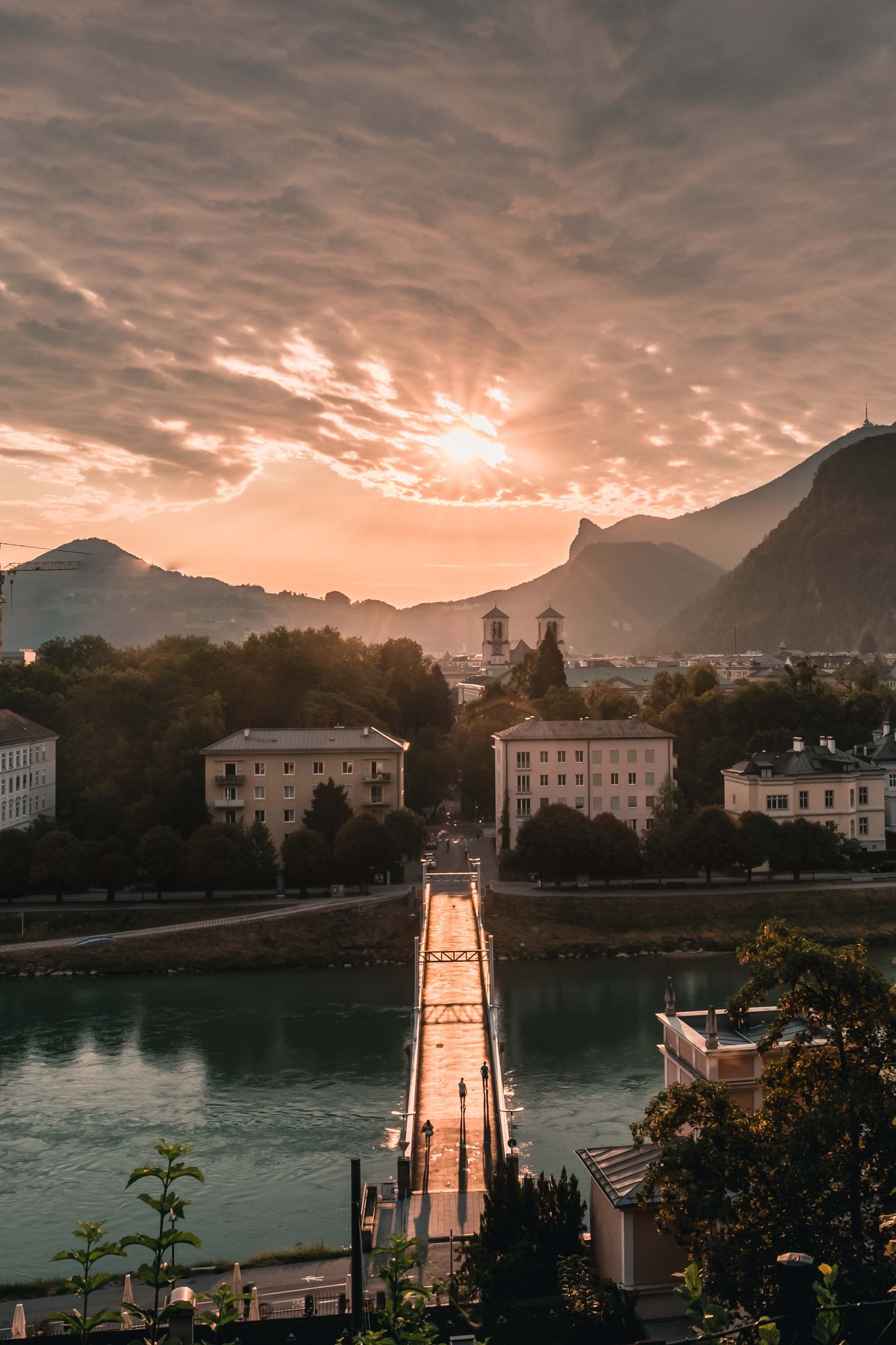 Footbridge Muellnersteg crosses the Salzach at sunrise with Gaisberg and Kapuzinerberg beyond.