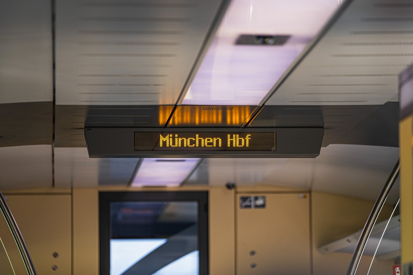 An amber LED display mounted under the ceiling of a train carriage reads Muenchen Hbf.