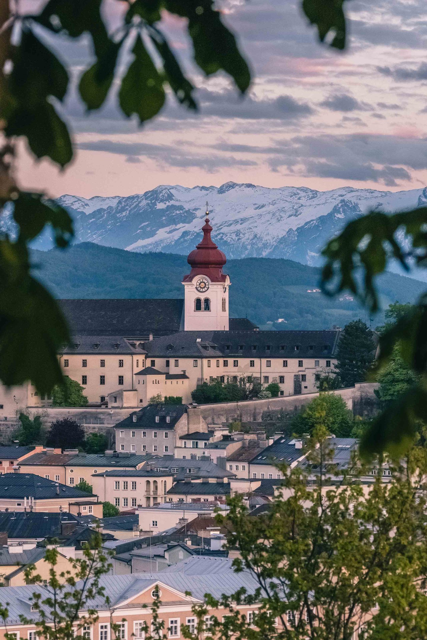 Nonnberg Abbey tower with snowy Alps behind framed by tree leaves in Salzburg.