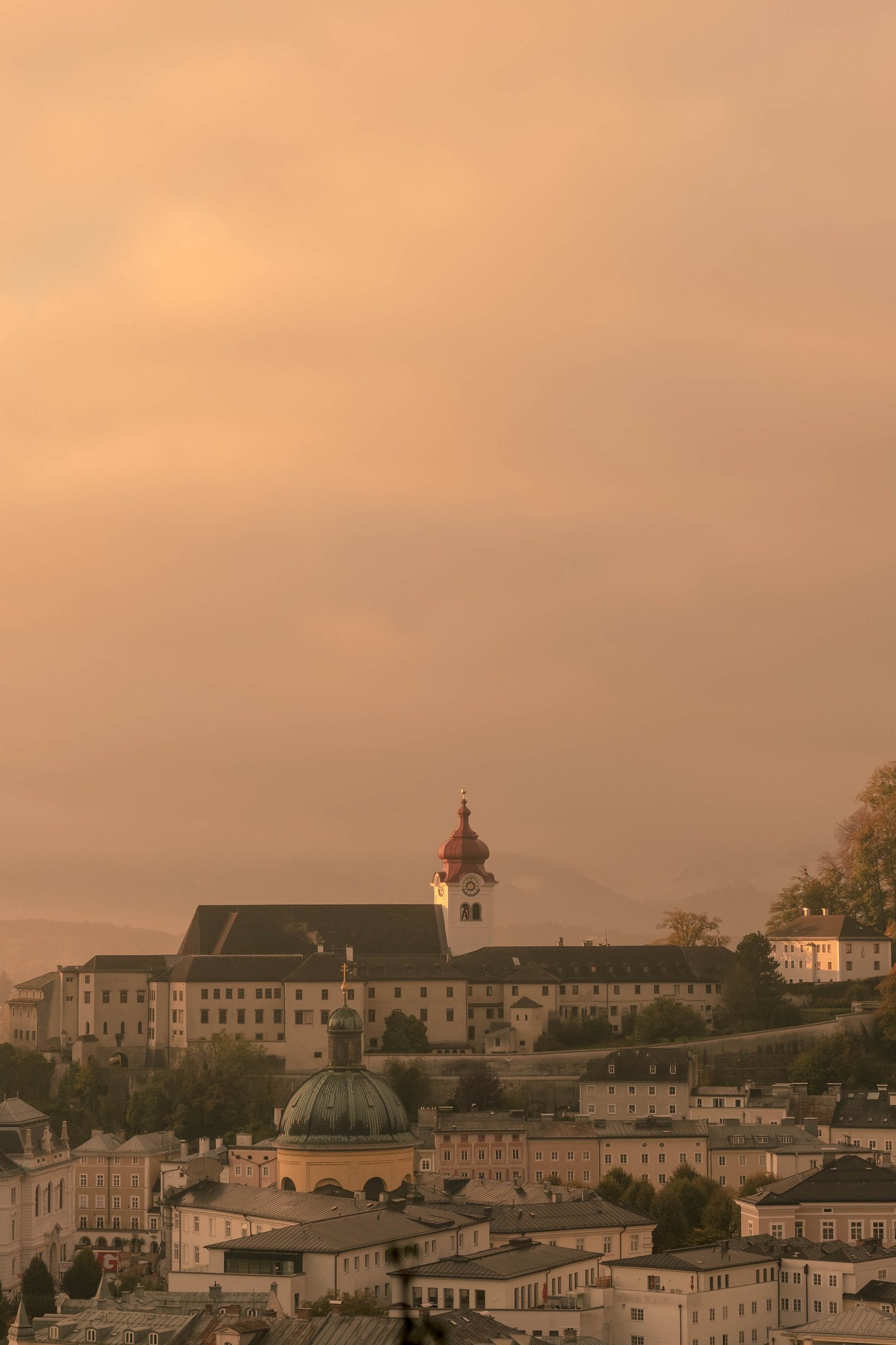 Nonnberg Abbey red-capped tower rising above Altstadt rooftops in hazy morning light in Salzburg.