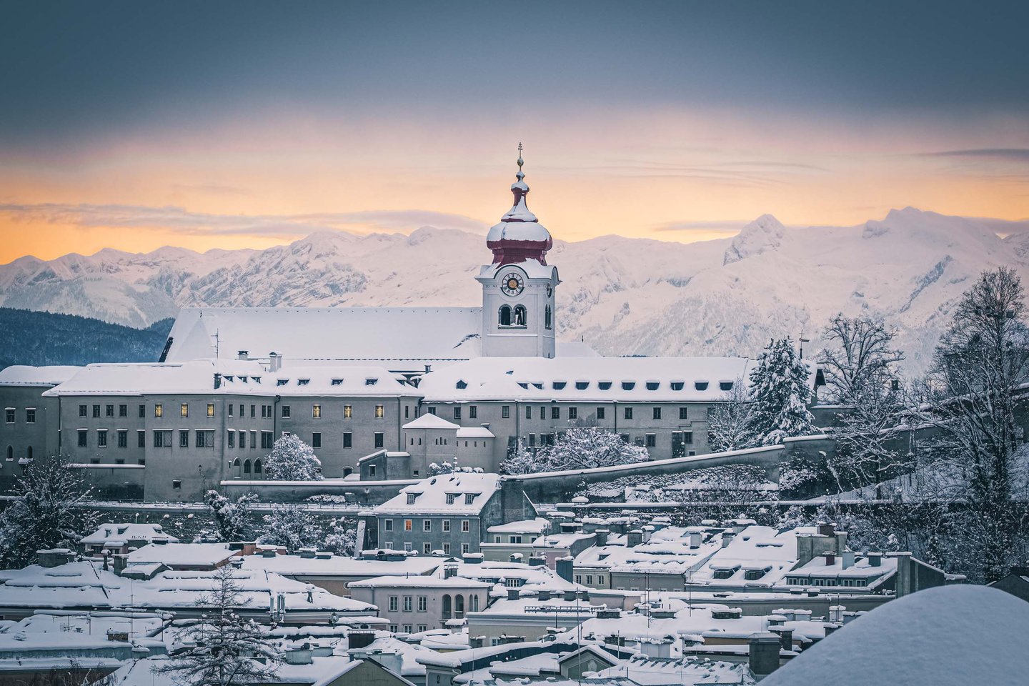 Nonnberg Abbey with snowy Alps behind at sunset seen across the Salzburg rooftops.