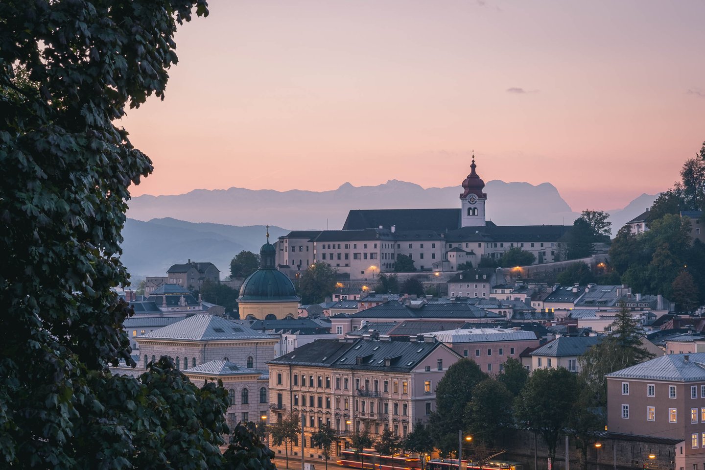 Nonnberg Abbey tower glowing above Altstadt rooftops with Alps on the horizon in Salzburg.
