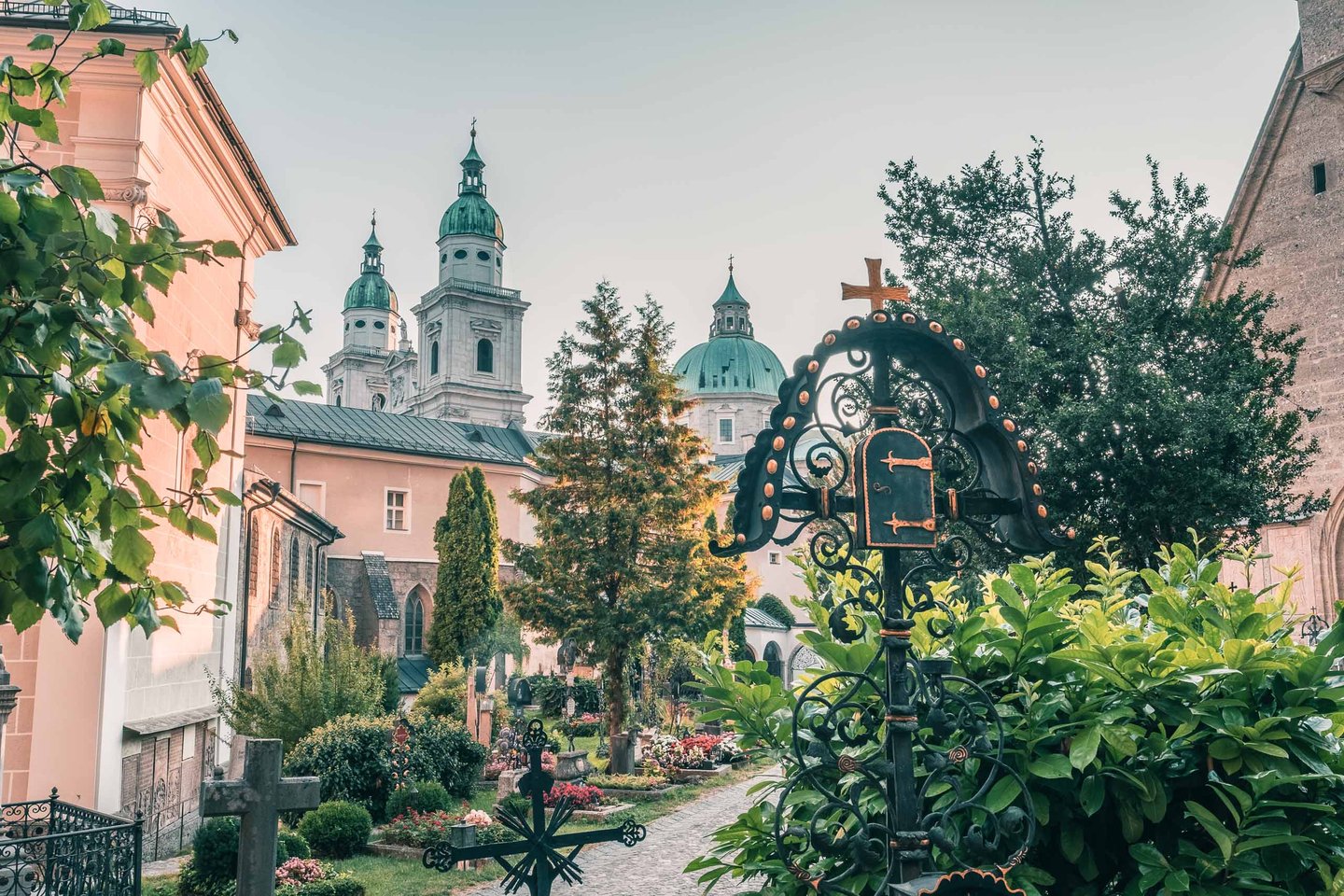 Wrought iron grave marker in St Peter cemetery with Salzburg Cathedral domes rising behind in Salzburg.