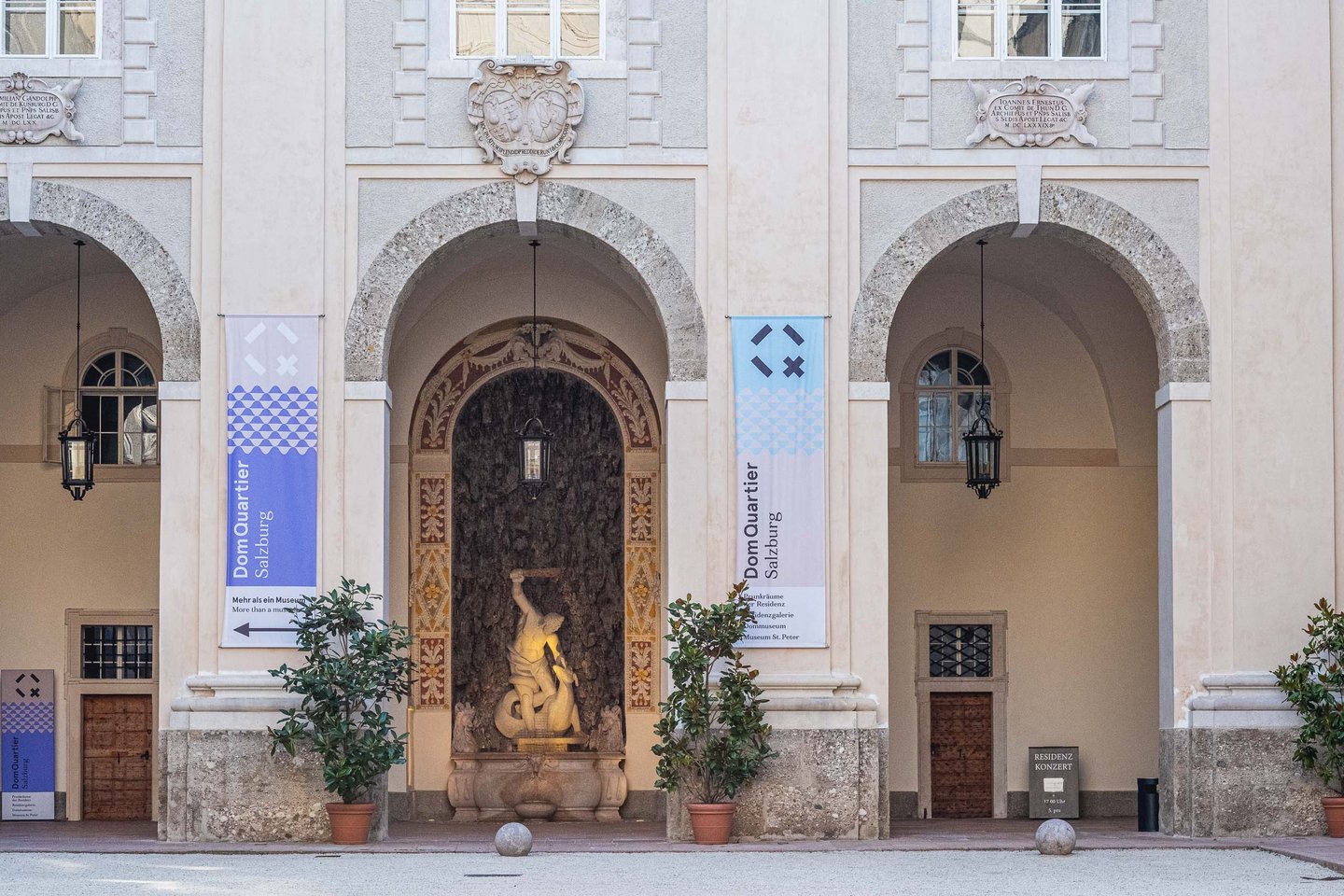Residenz courtyard archway with DomQuartier banners and wall fountain sculpture in Salzburg