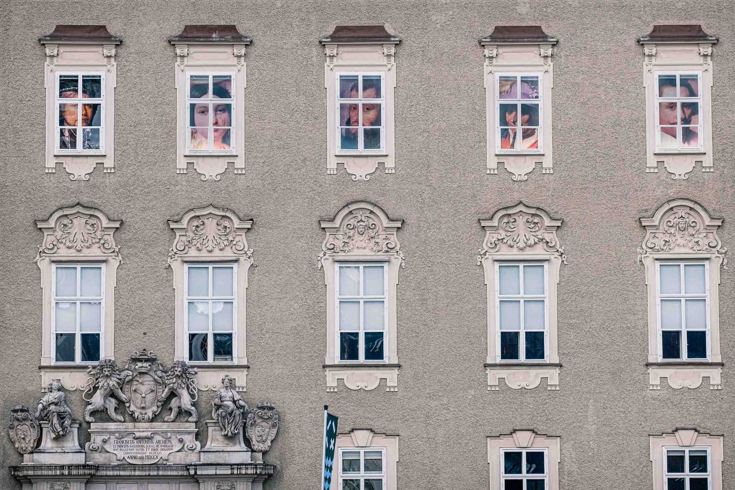 Old Residenz facade with historic portraits in windows and lion crest above entrance in Salzburg.