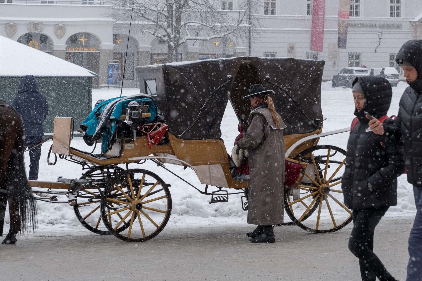 A horse drawn fiaker carriage waits on Residenzplatz during snowfall in Salzburg old town.