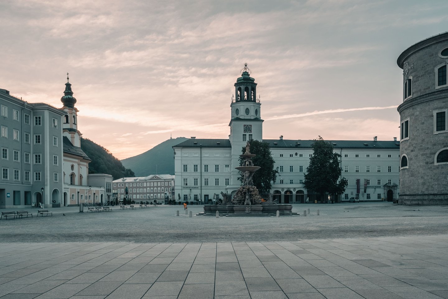 Empty Residenzplatz with fountain and Glockenspiel tower of the Neue Residenz at sunrise in Salzburg.