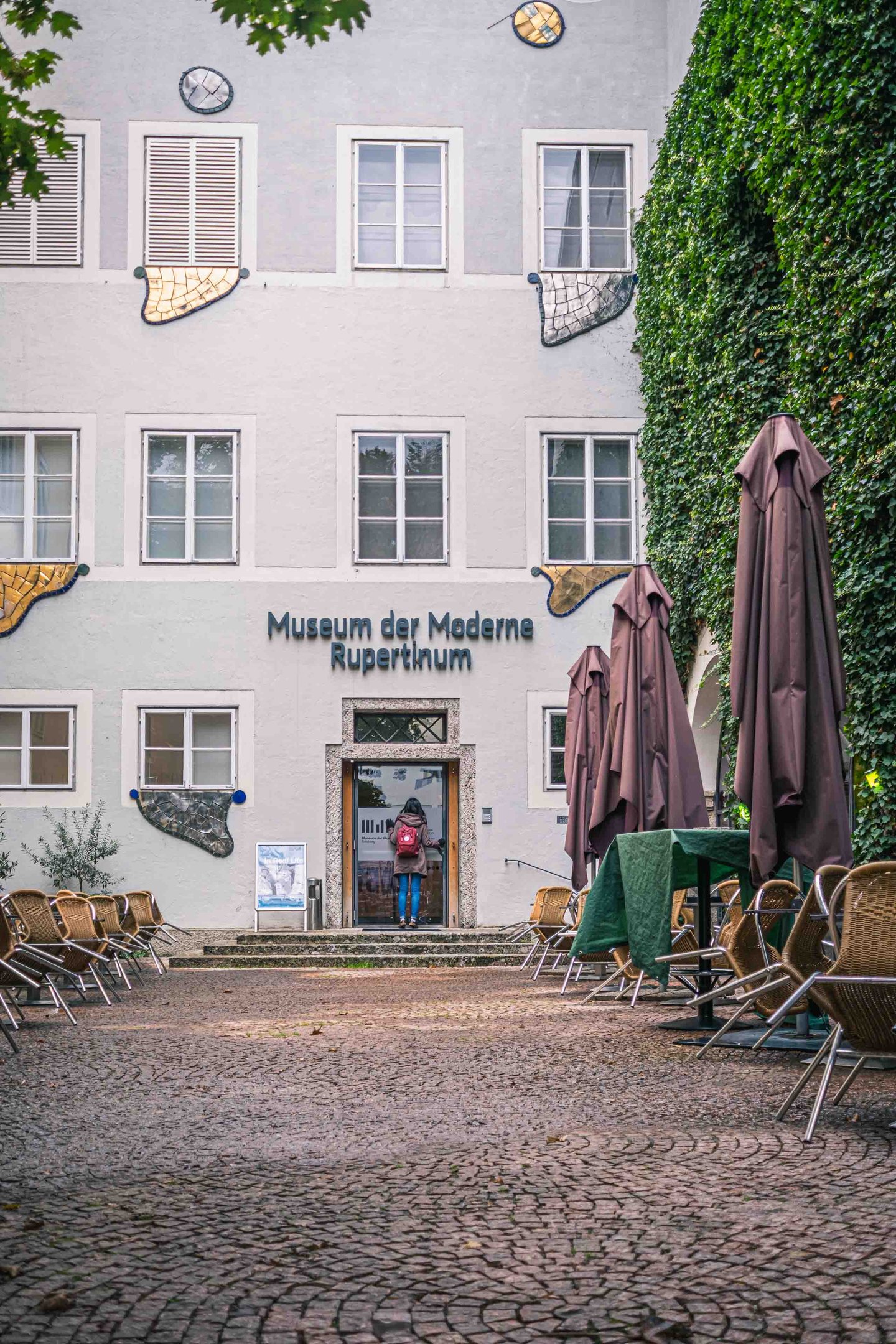 A visitor enters the Museum der Moderne Rupertinum past empty cafe seating in Salzburg old town.