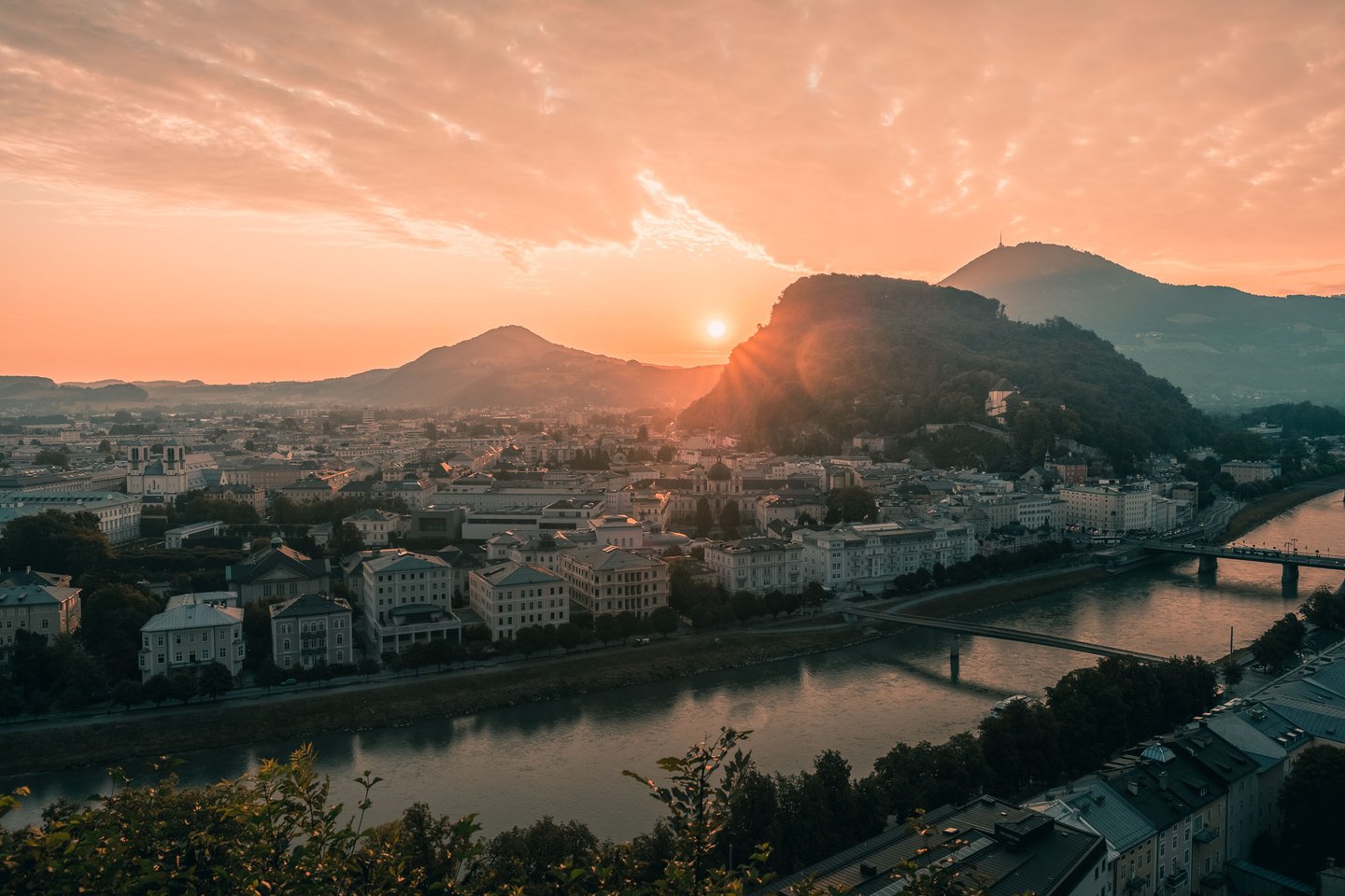 Sun rises between Kapuzinerberg and Gaisberg above the Salzach in Salzburg.
