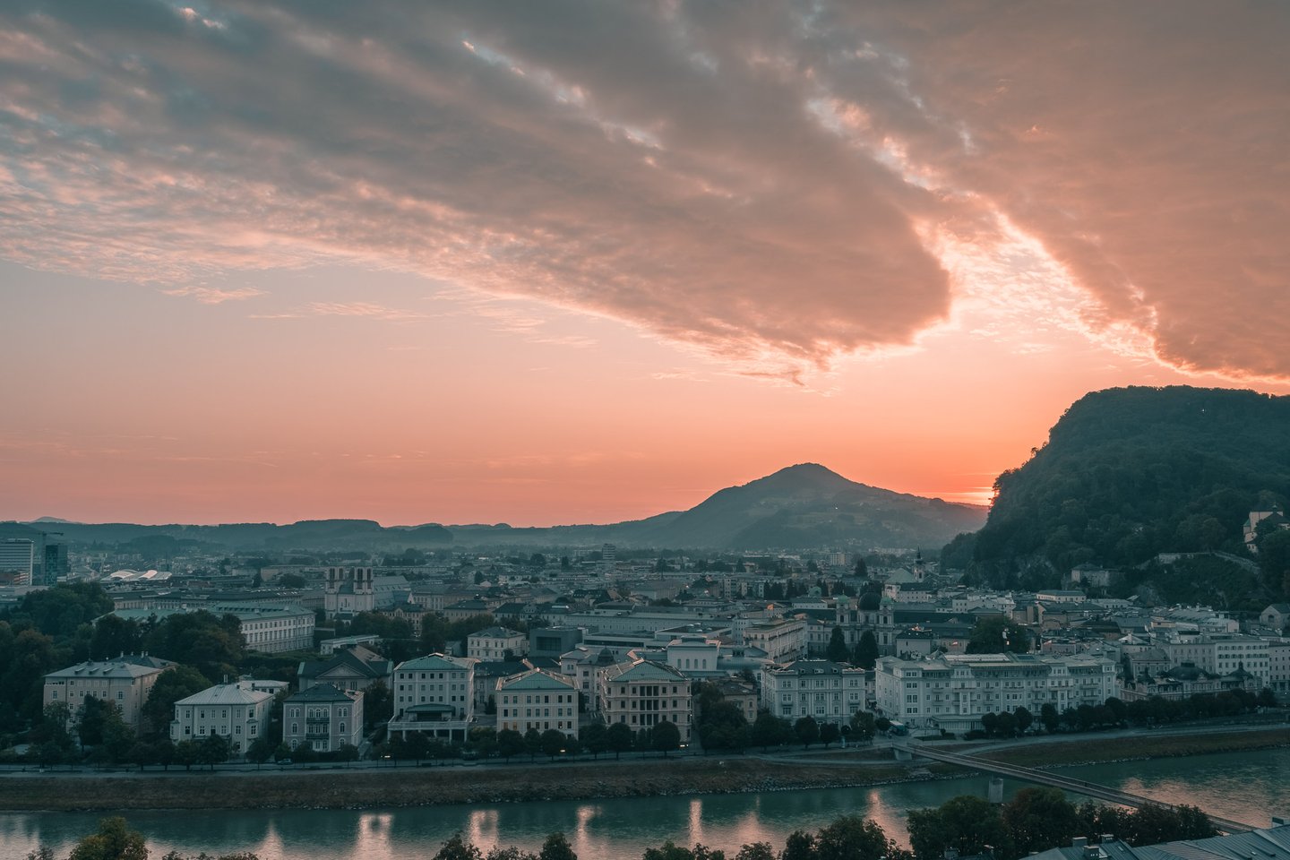 Warm sunrise over Salzburg Neustadt rooftops with Kapuzinerberg rising on the right.