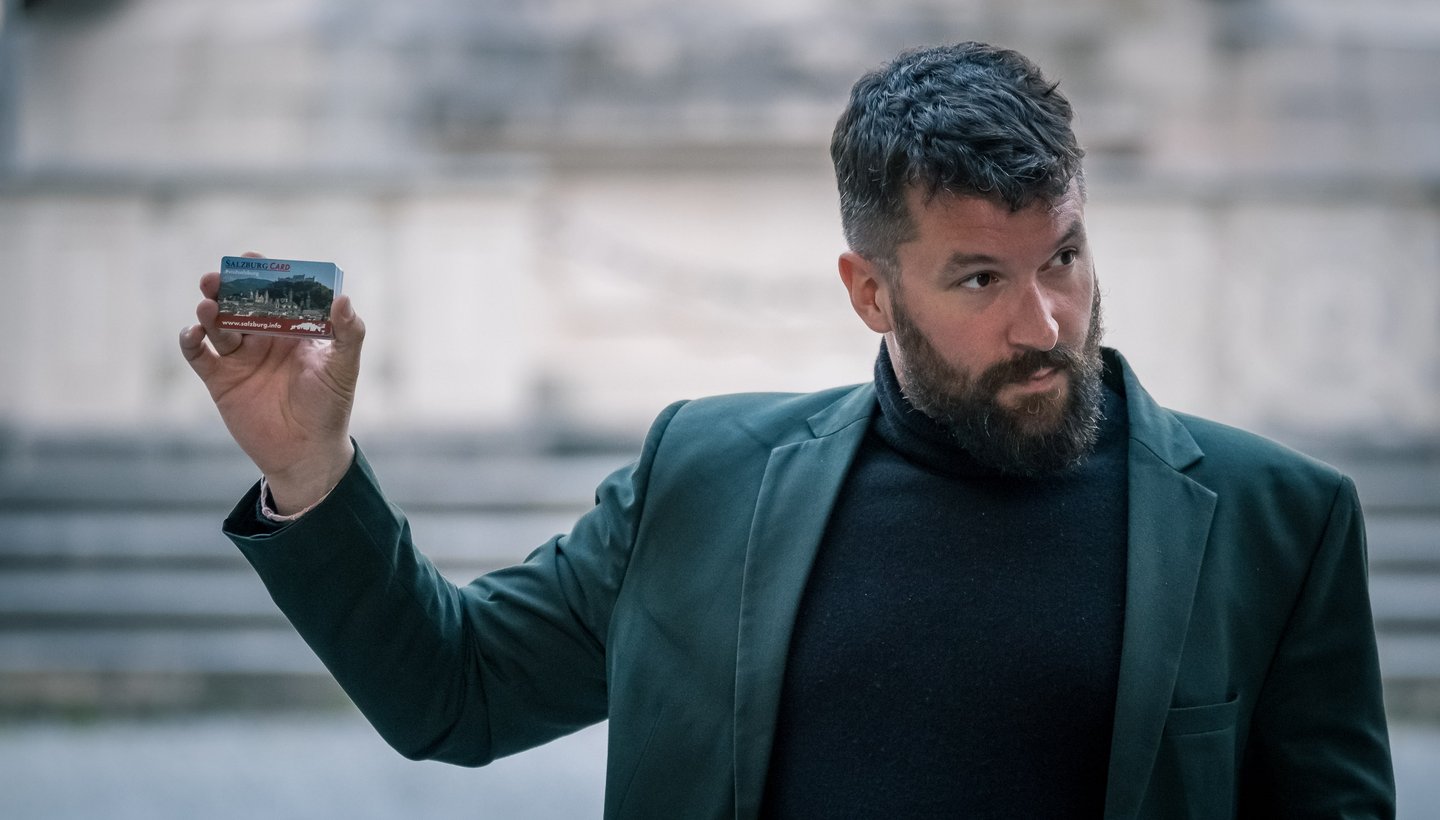 Bearded man in dark coat holds a Salzburg Card in a Salzburg old town alley