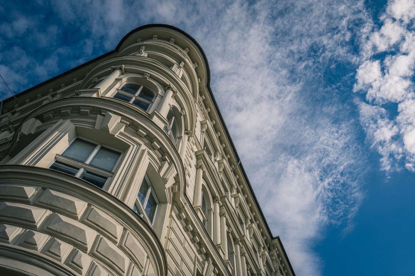 Ornate historicist corner building facade with bay windows rises against a blue cloudy sky in Salzburg.