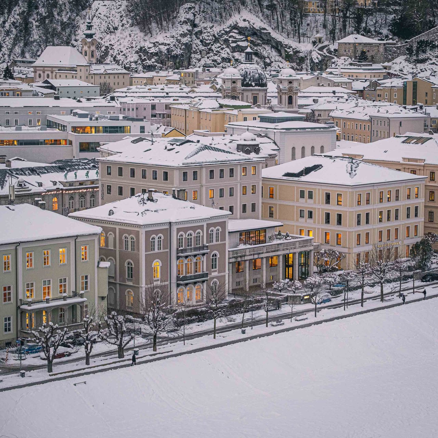 Illuminated grand facades line the Elisabethkai along the Salzach at winter dusk in Salzburg Neustadt.