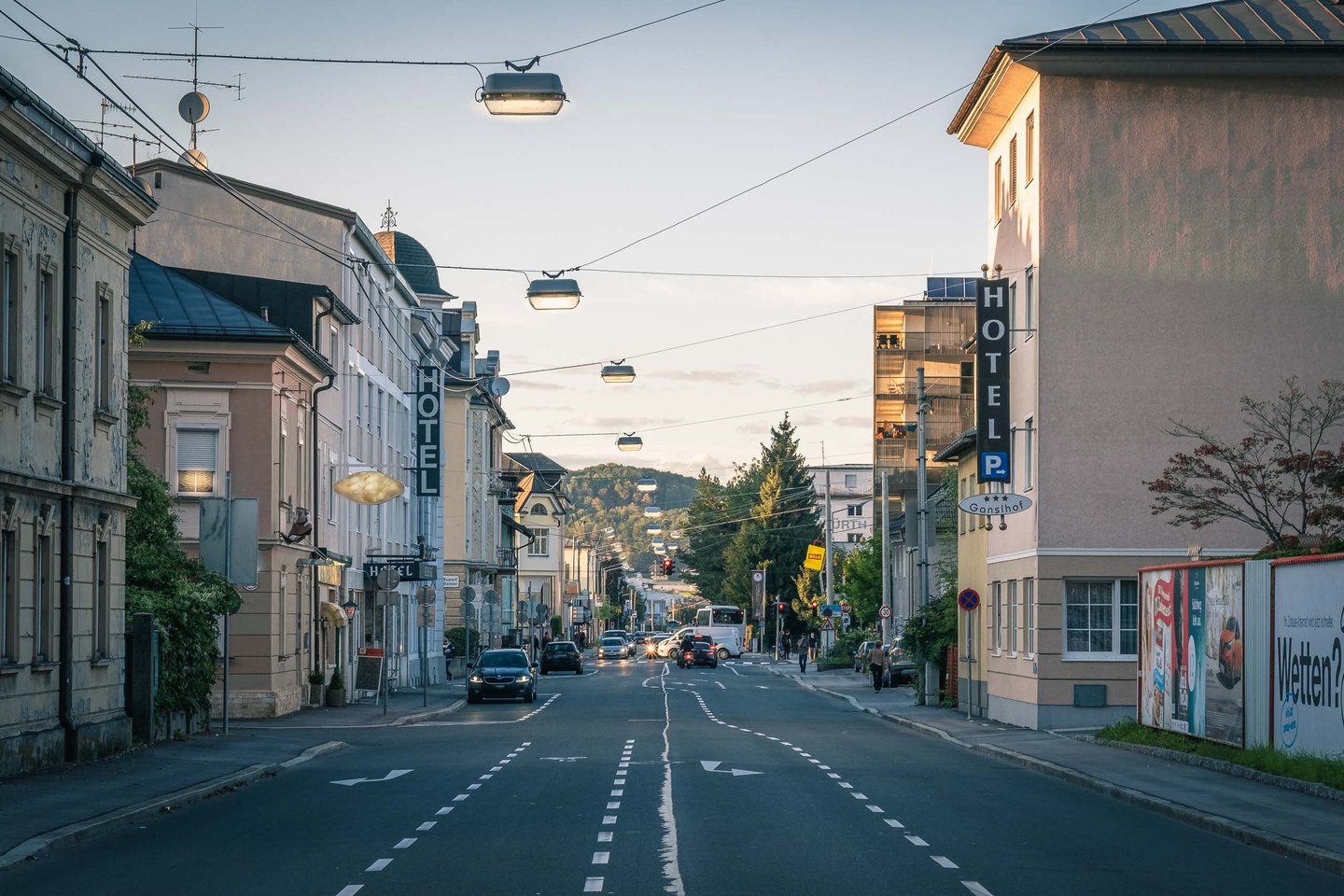 Hotel signs line a quiet Neustadt street at dusk with the Kapuzinerberg visible in Salzburg.
