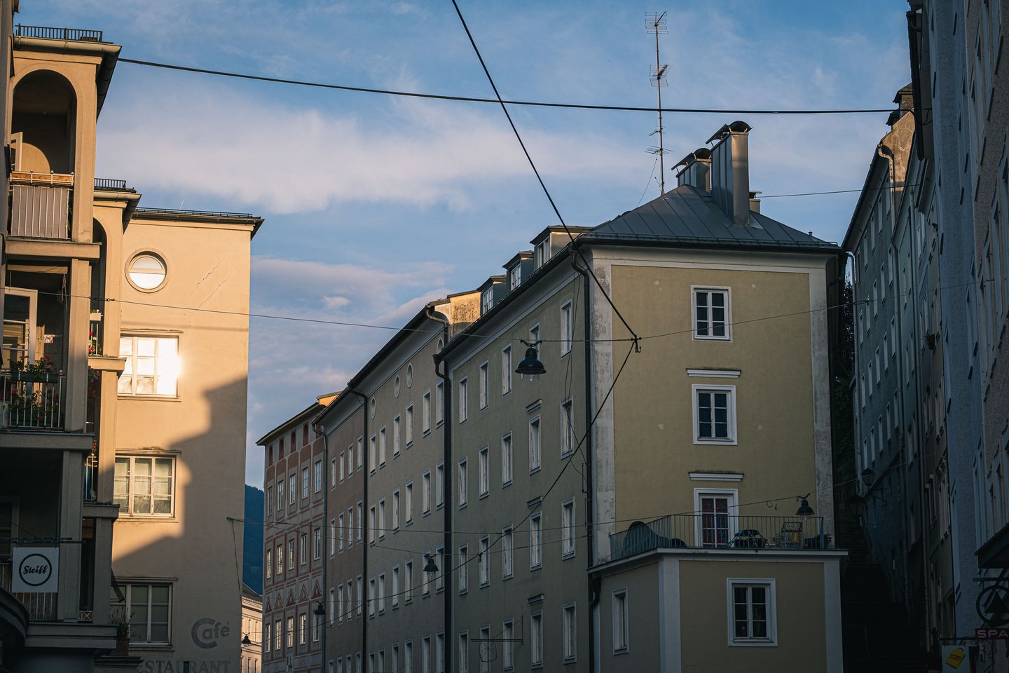 Pastel Nonntal facades and rooftops at sunset with a Cafe sign on a balcony in Salzburg.