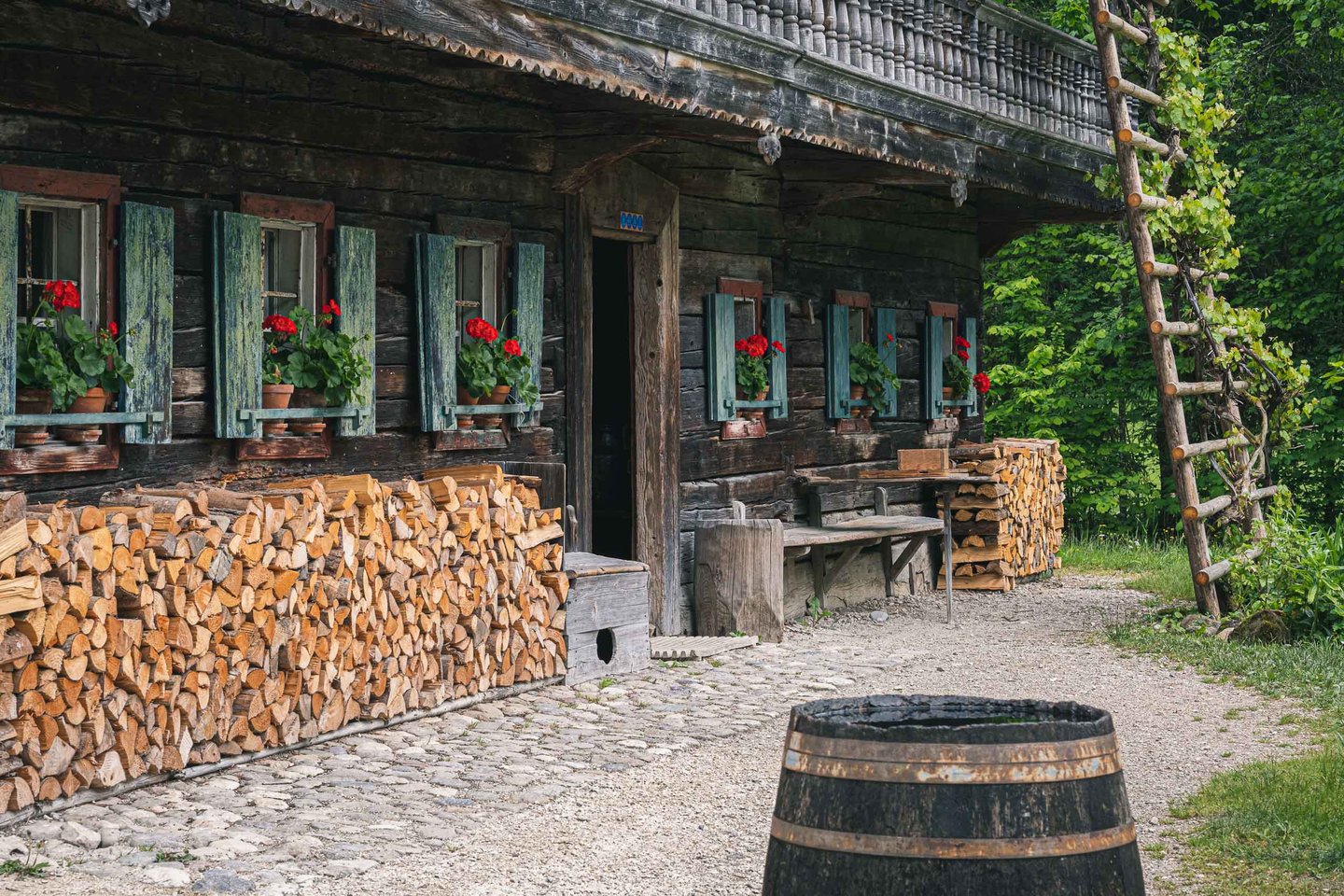 Farmhouse facade with geraniums and stacked firewood and wooden barrel at Salzburger Freilichtmuseum in Grossgmain