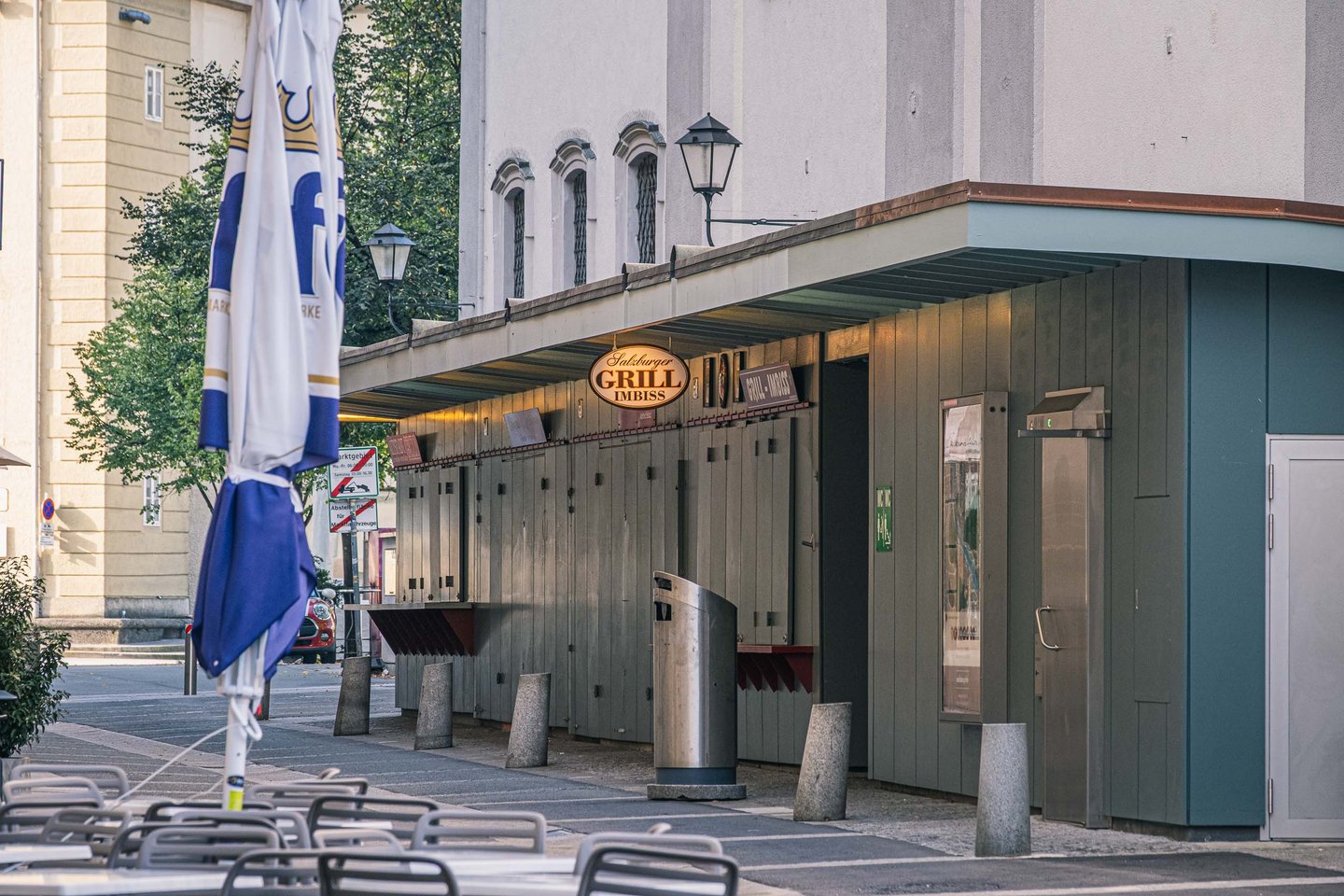 Exterior of the Salzburger Grill Imbiss kiosk with a Stiegl-branded umbrella beside the green wooden hut