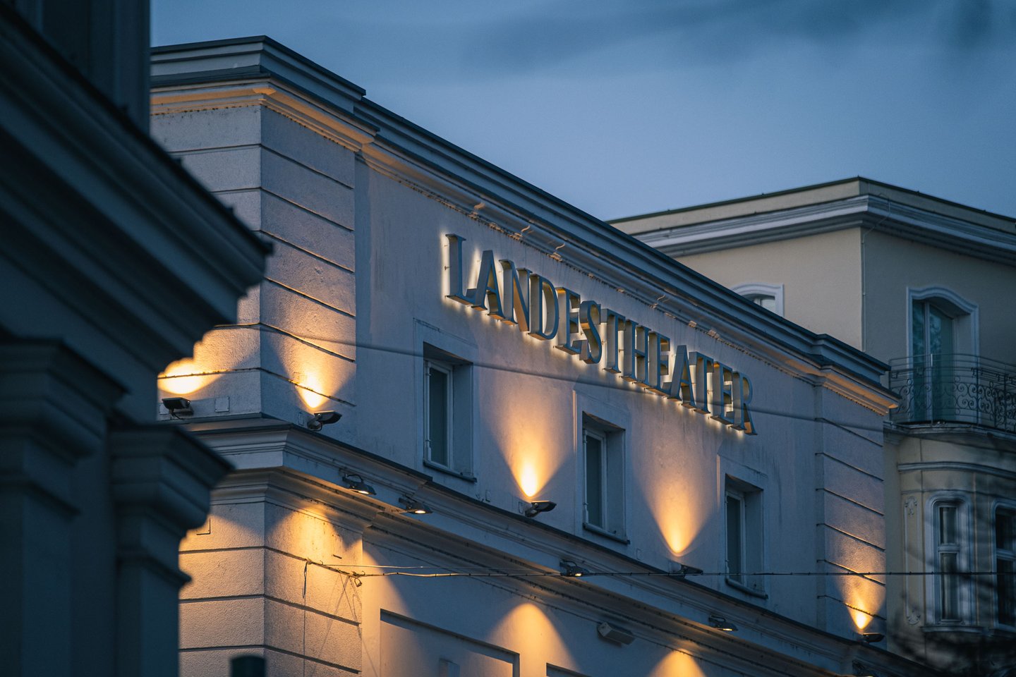 Illuminated LANDESTHEATER lettering on the facade of Salzburg state theater at dusk.