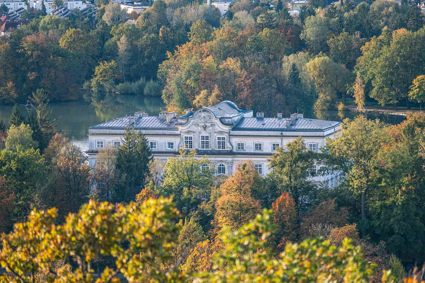 Schloss Leopoldskron palace framed by autumn foliage with its pond and surrounding forest in Salzburg.