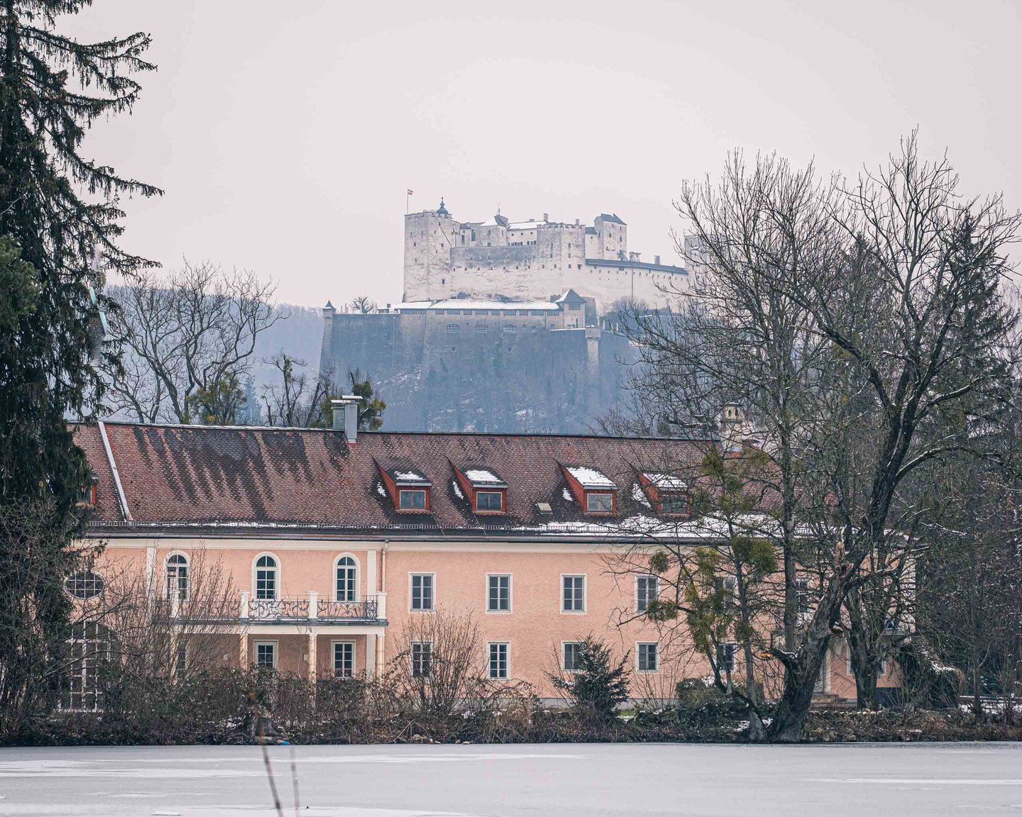 Schloss Leopoldskron outbuilding with Hohensalzburg Fortress rising behind in winter in Salzburg.