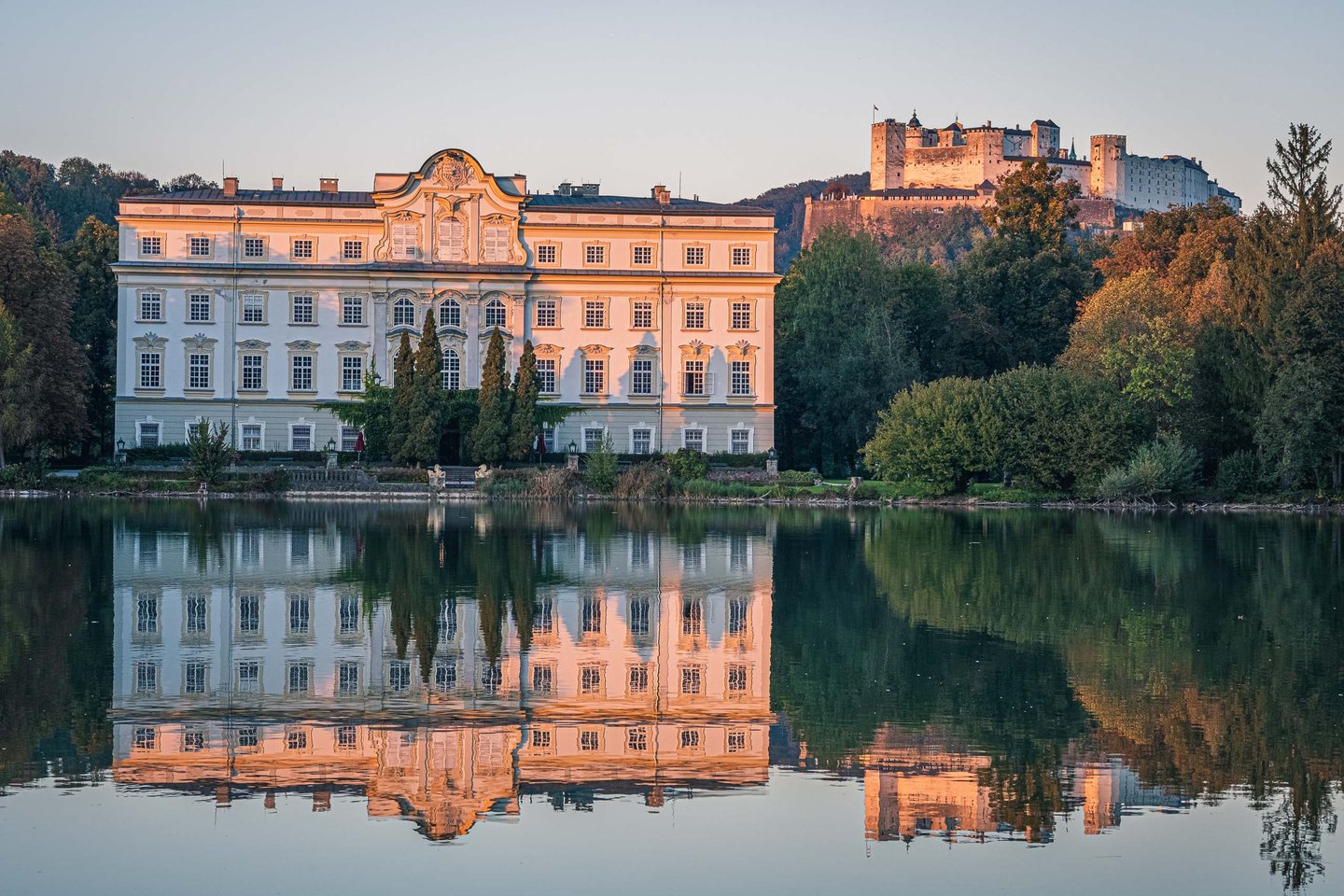 Schloss Leopoldskron reflected in Leopoldskroner Weiher with Hohensalzburg fortress at sunset