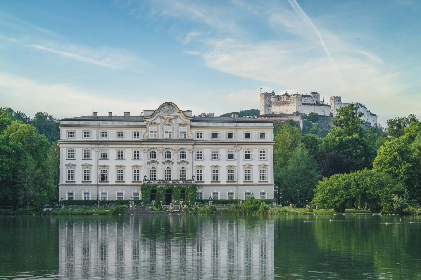 Schloss Leopoldskron reflected in Leopoldskroner Weiher with Hohensalzburg Fortress behind in Salzburg