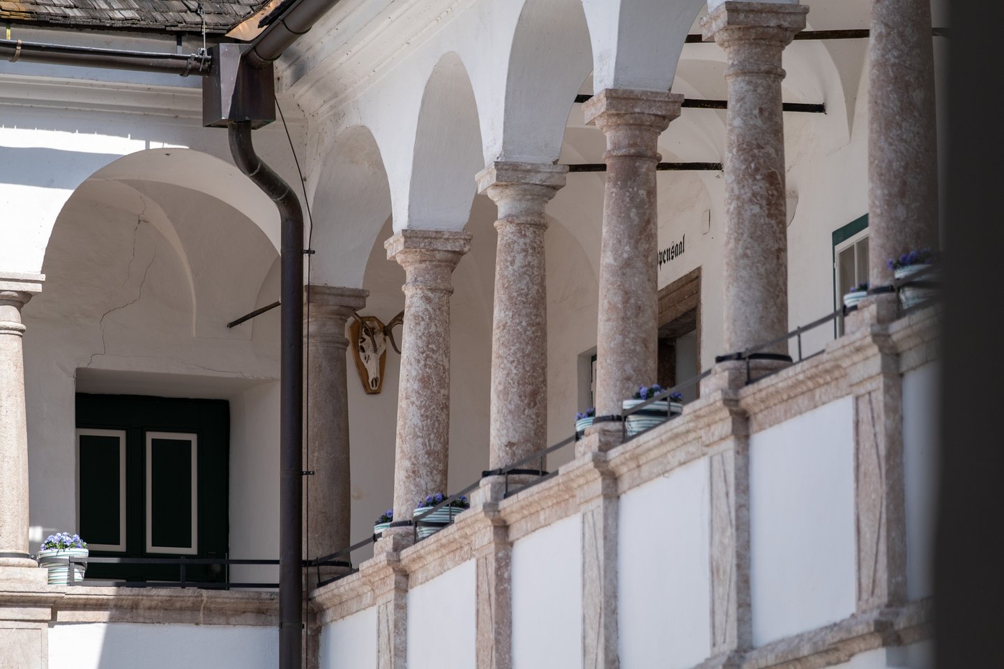 The arcaded upper gallery of the Renaissance courtyard at Seeschloss Ort, with rough marble columns, flower boxes on the rail, a mounted skull and the doorway to the Wappensaal.