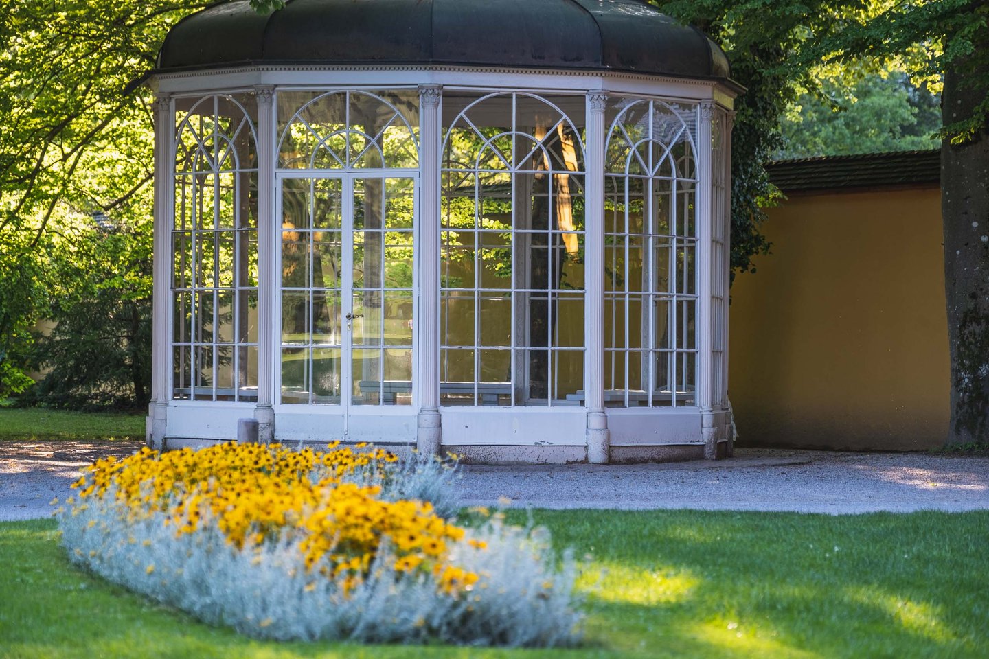 Glass Sound of Music pavilion with yellow flower bed in the Hellbrunn palace garden.